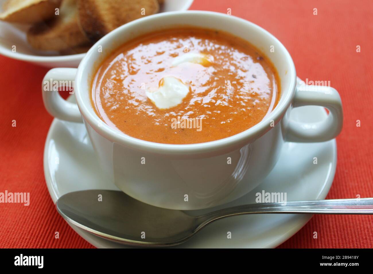 Tomato cream soup hot orange color close up view on bright red background. Selective focus. Copy space Stock Photo