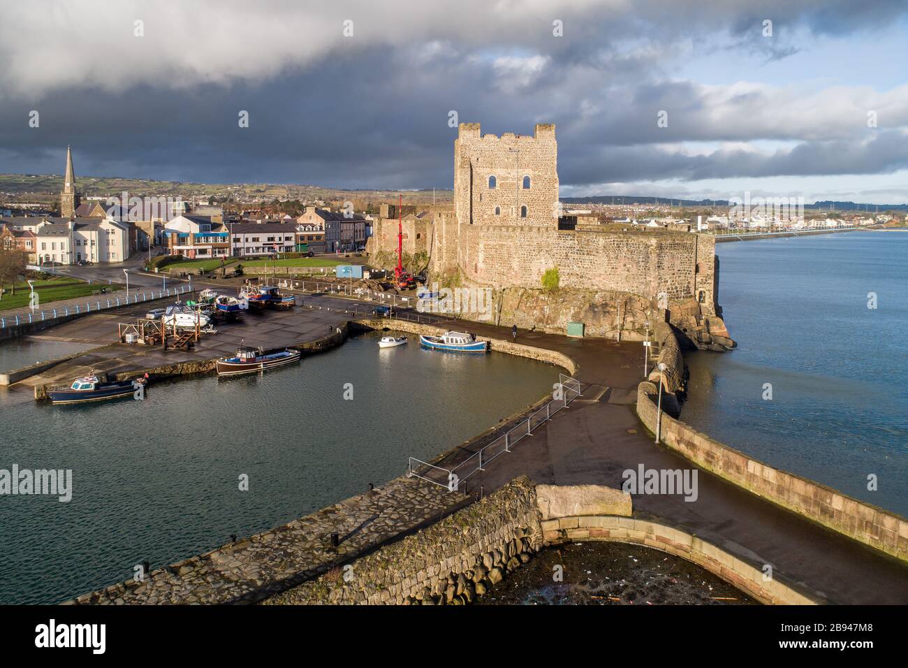 Medieval Norman Castle, harbor with boat ramp and wave breaker in Carrickfergus near Belfast, Northern Ireland, UK. Aerial view in sunset light Stock Photo