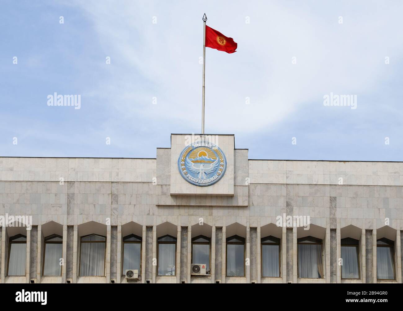 Kyrgyzstan White House with the government emblem featuring the Tulip Revolution logo. Parliament of the Kyrgyz Republic in Bishkek and flag. Stock Photo