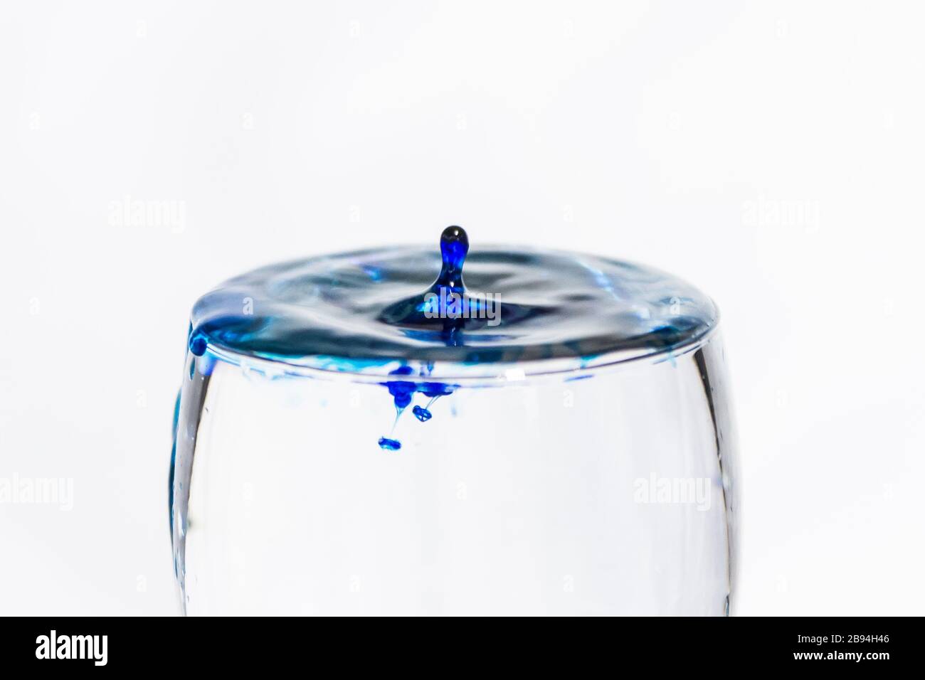 Blue drop splashing into a clear glass of water Stock Photo