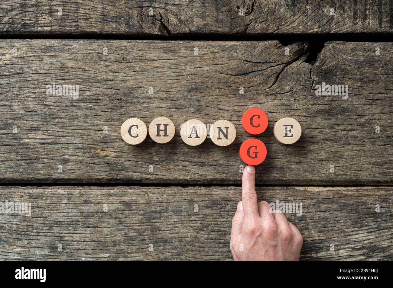 Word Chance spelled on wooden cut circles with male hand pusing in letter G to change it into Change. Stock Photo