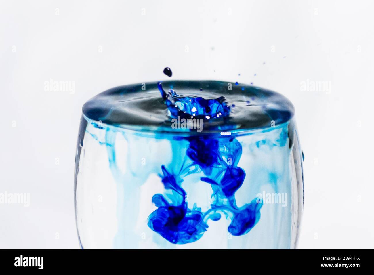 Blue drop splashing into a clear glass of water Stock Photo