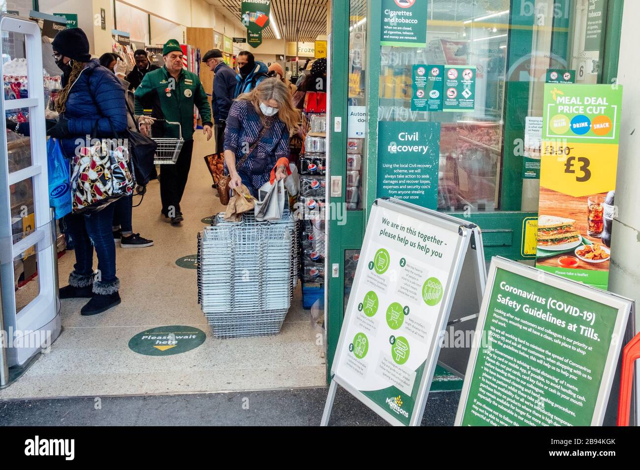 Camberwell, London, UK. 23rd March, 2020. Signs giving advice on Coronavirus and asking people to be considerate at Morrisons Supermarket.  A shopper wears a facemask to help prevent the risk of infection from Coronavirus. Credit: Tom Leighton/Alamy Live News Stock Photo