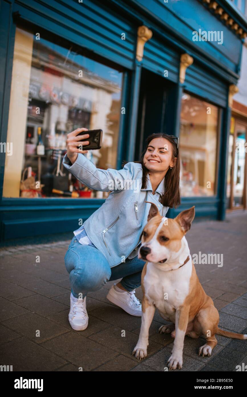 A beautiful young girl on the street taking photos of herself and her dog Stock Photo