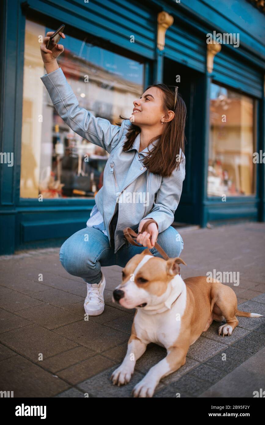 A beautiful young girl on the street taking photos of herself and her dog Stock Photo