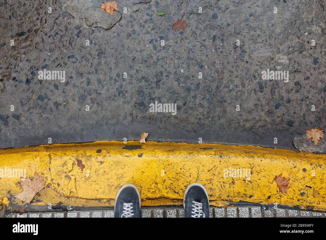Feet on yellow painted sidewalk curb during a rainig day in Buenos Aires Stock Photo