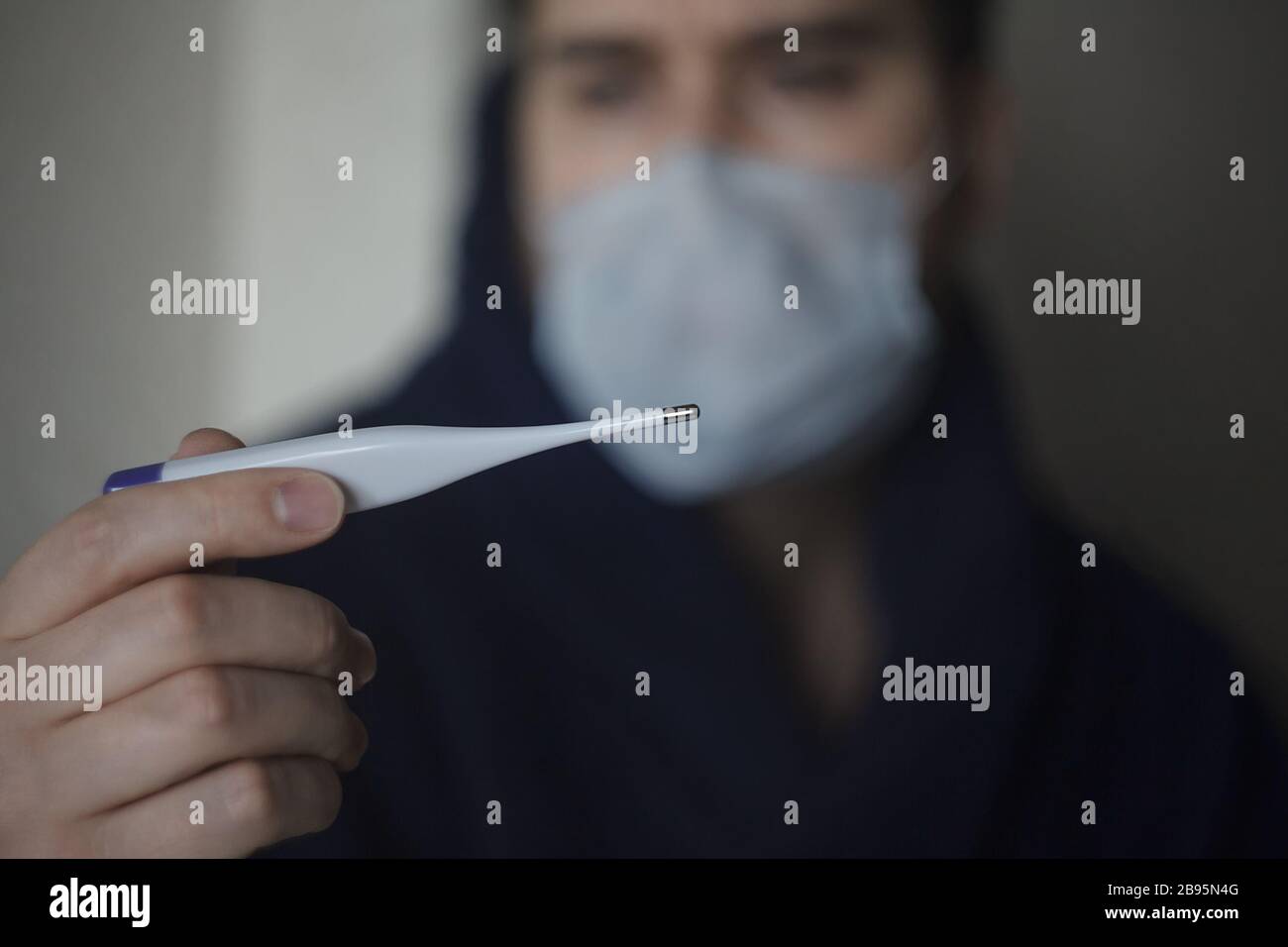 Blurred man in medicine mask holding thermometer in front of him Stock Photo