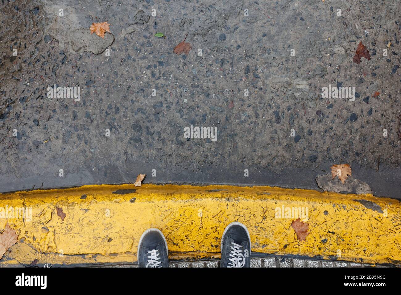 Feet on yellow painted sidewalk curb during a rainig day in Buenos Aires Stock Photo