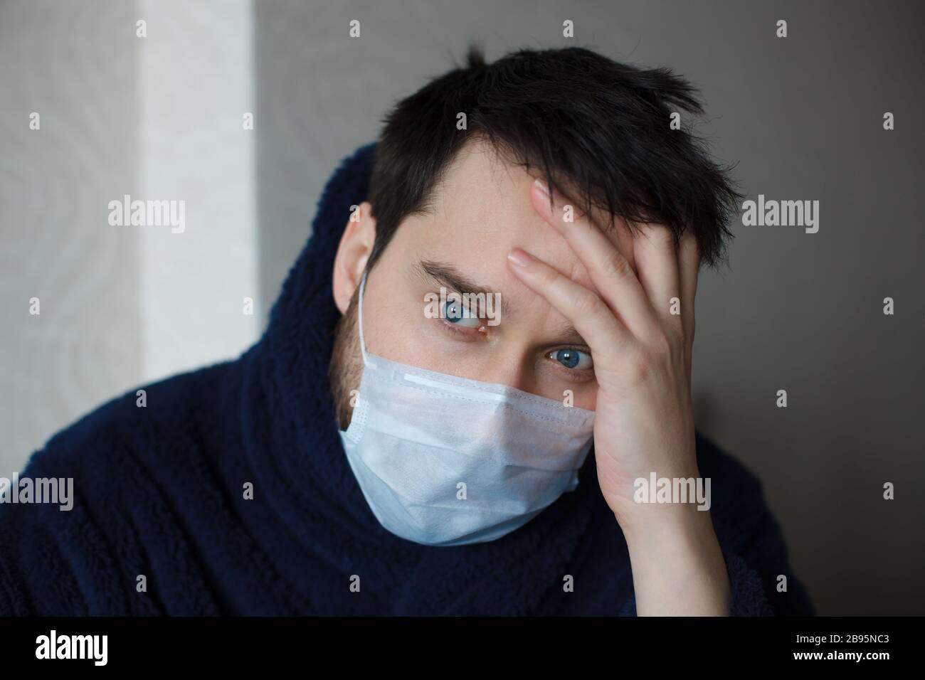 Overhelmed man in medicine mask with his hand on a forhead. How to stay calm during coronavirus pandemic Stock Photo