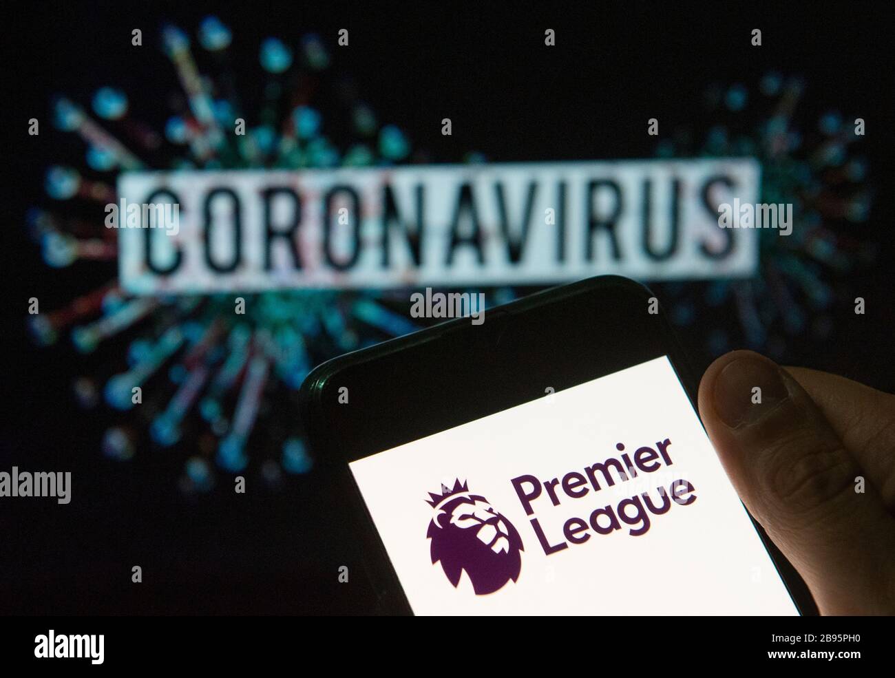 In this photo illustration the top level of the English football league Premier League logo seen displayed on a smartphone with a computer model of the COVID-19 coronavirus on the background. Stock Photo
