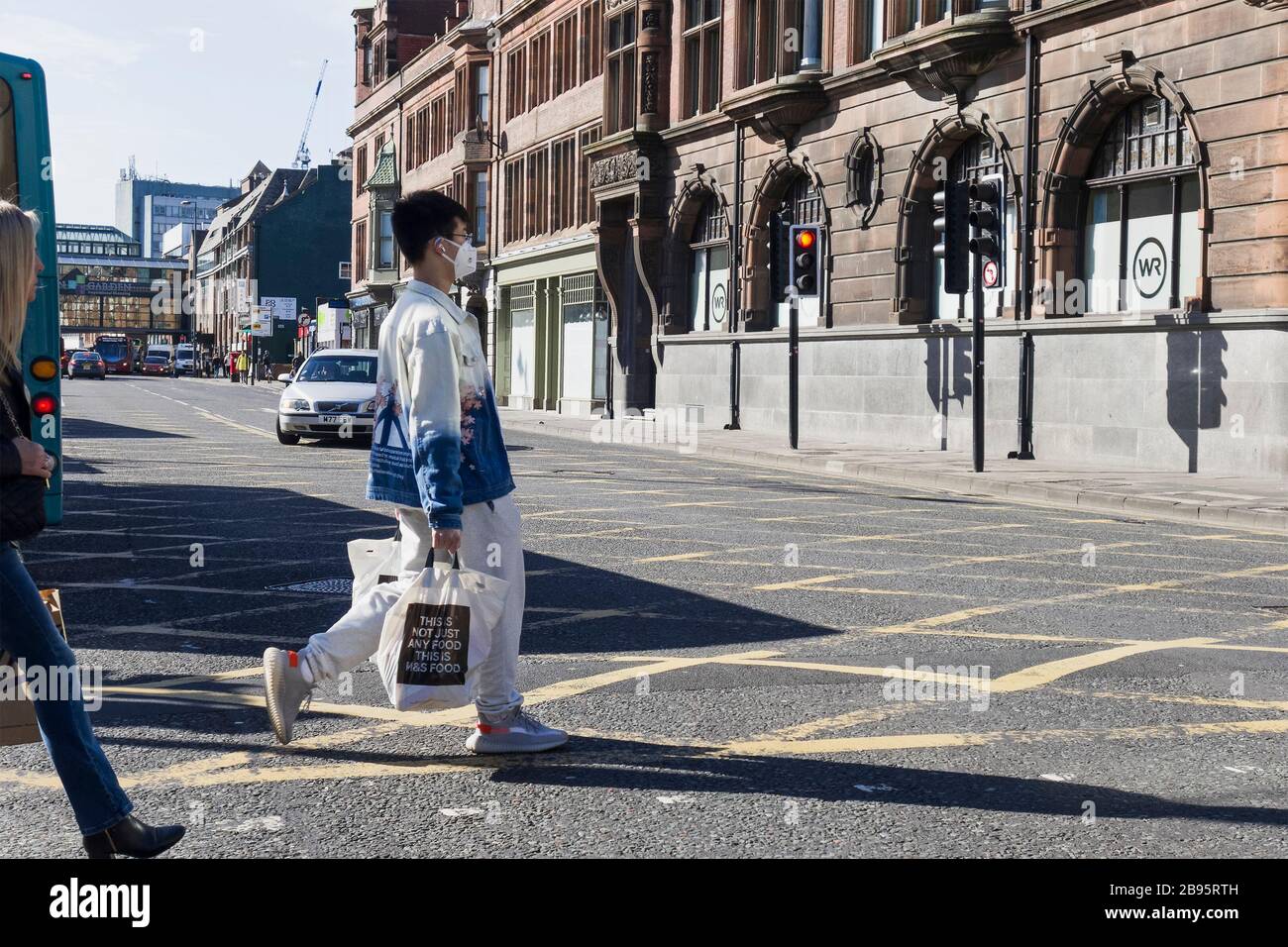 An Asian man crosses a Haymarket road in Newcastle upon Tyne, UK, wearing a facemask as protection against covid-19, coronavirus puring the pandemic o Stock Photo