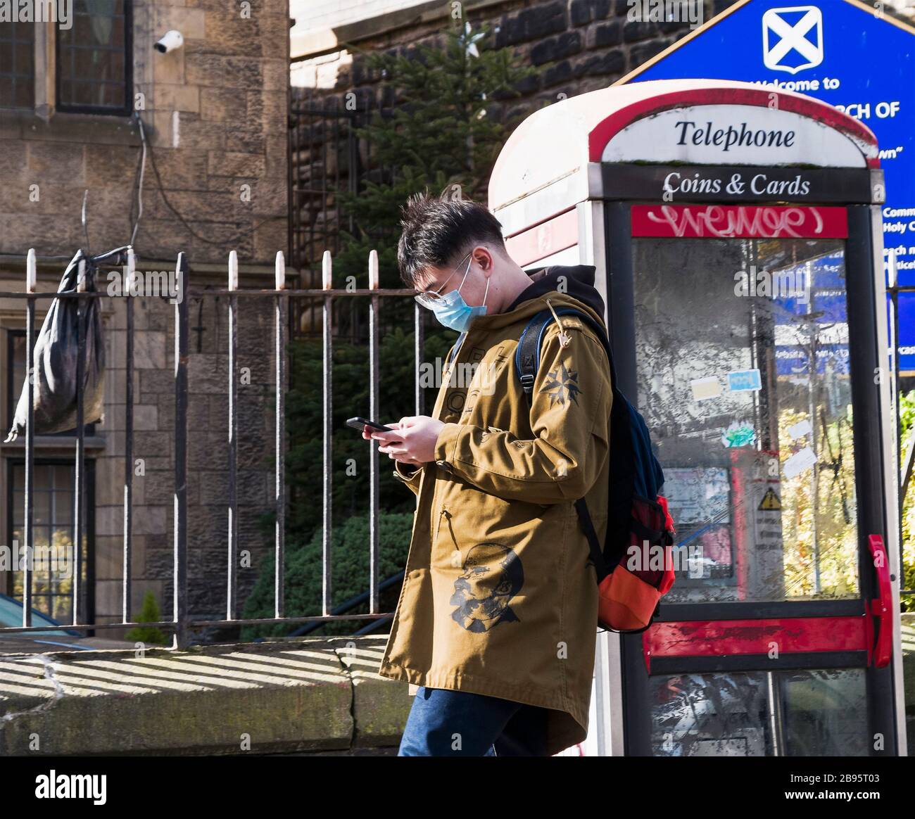 An asian male checks his smartphone while wearing a mask as protection against covid-19 on a Newcastle upon Tyne street, UK, during the 2020 pandemic. Stock Photo