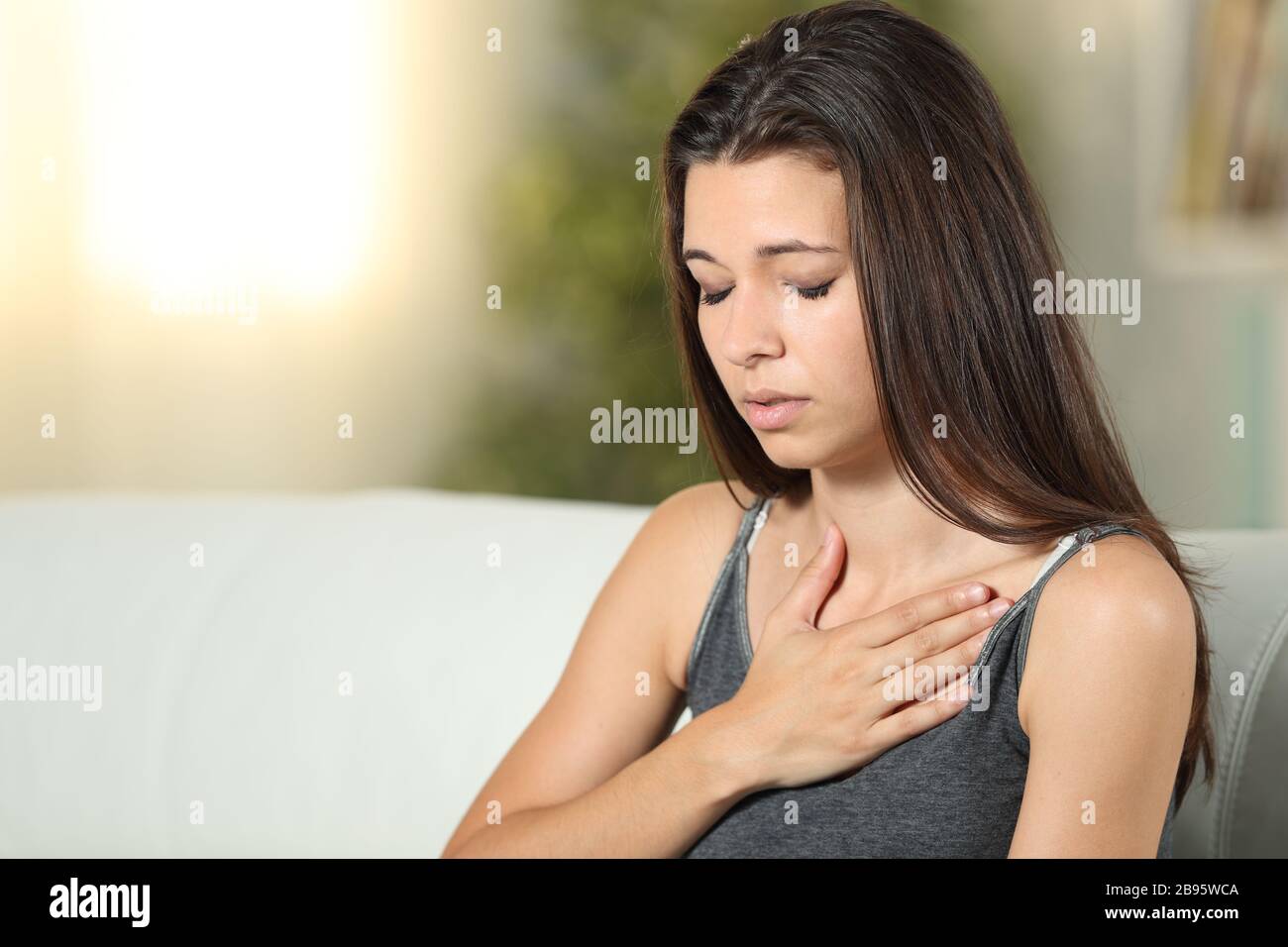 Girl having respiration problems touching chest sitting on a couch in the living room at home Stock Photo