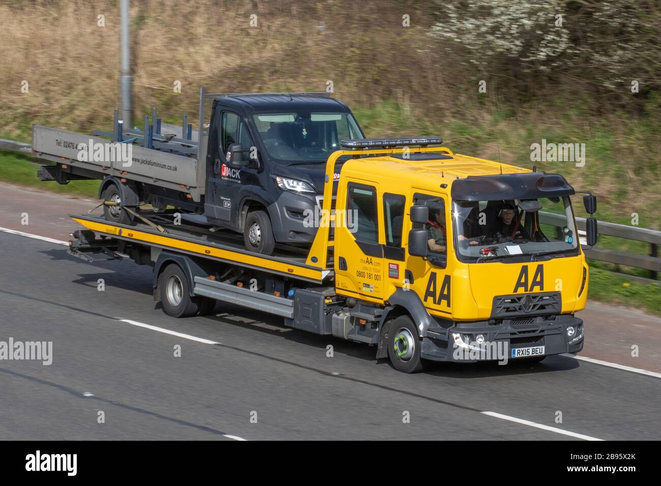 AA Double cab Van recovery truck carrying broken down van; Side view of rescue breakdown recovery roadside recovery lorry truck transporter transporting unmarked black van driving along  M6, Lancaster, UK; Vehicular traffic, transport, modern, on the 3 lane highway. Stock Photo