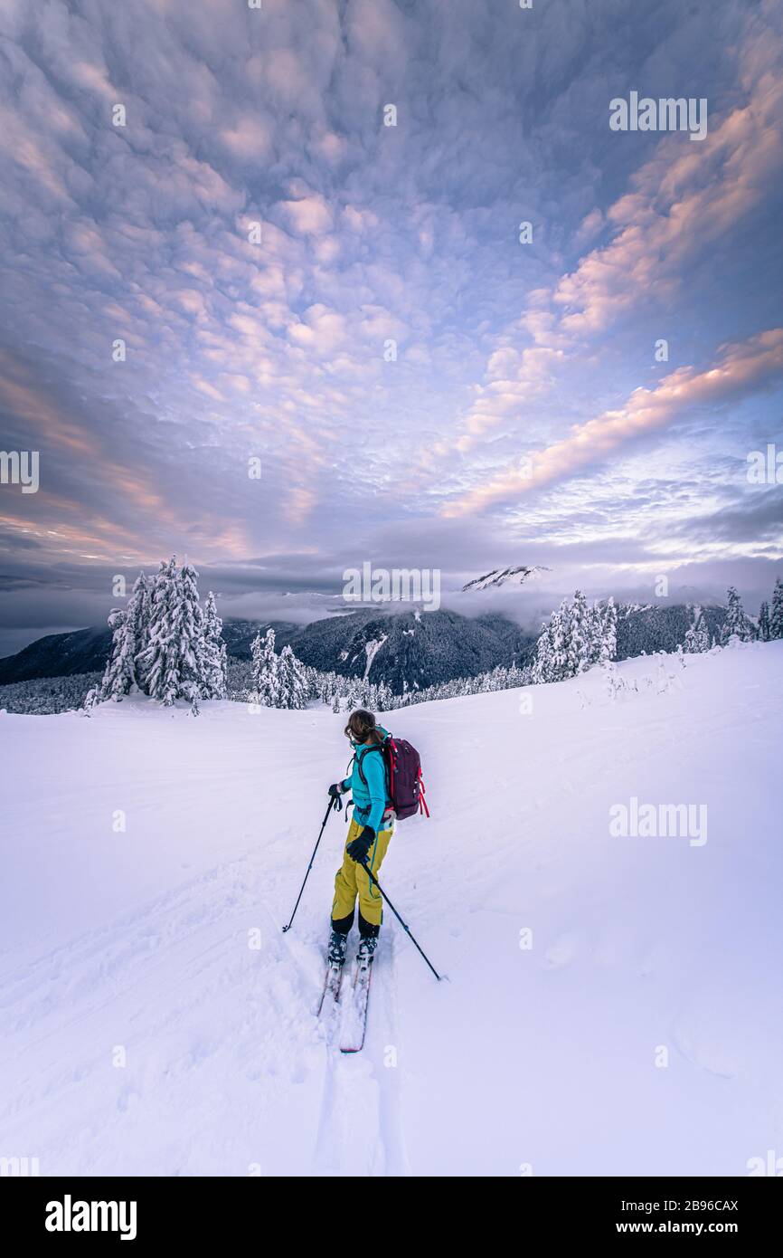 Person skiing through a wintry landscape, mountains in the distance, dramatic sky. Stock Photo