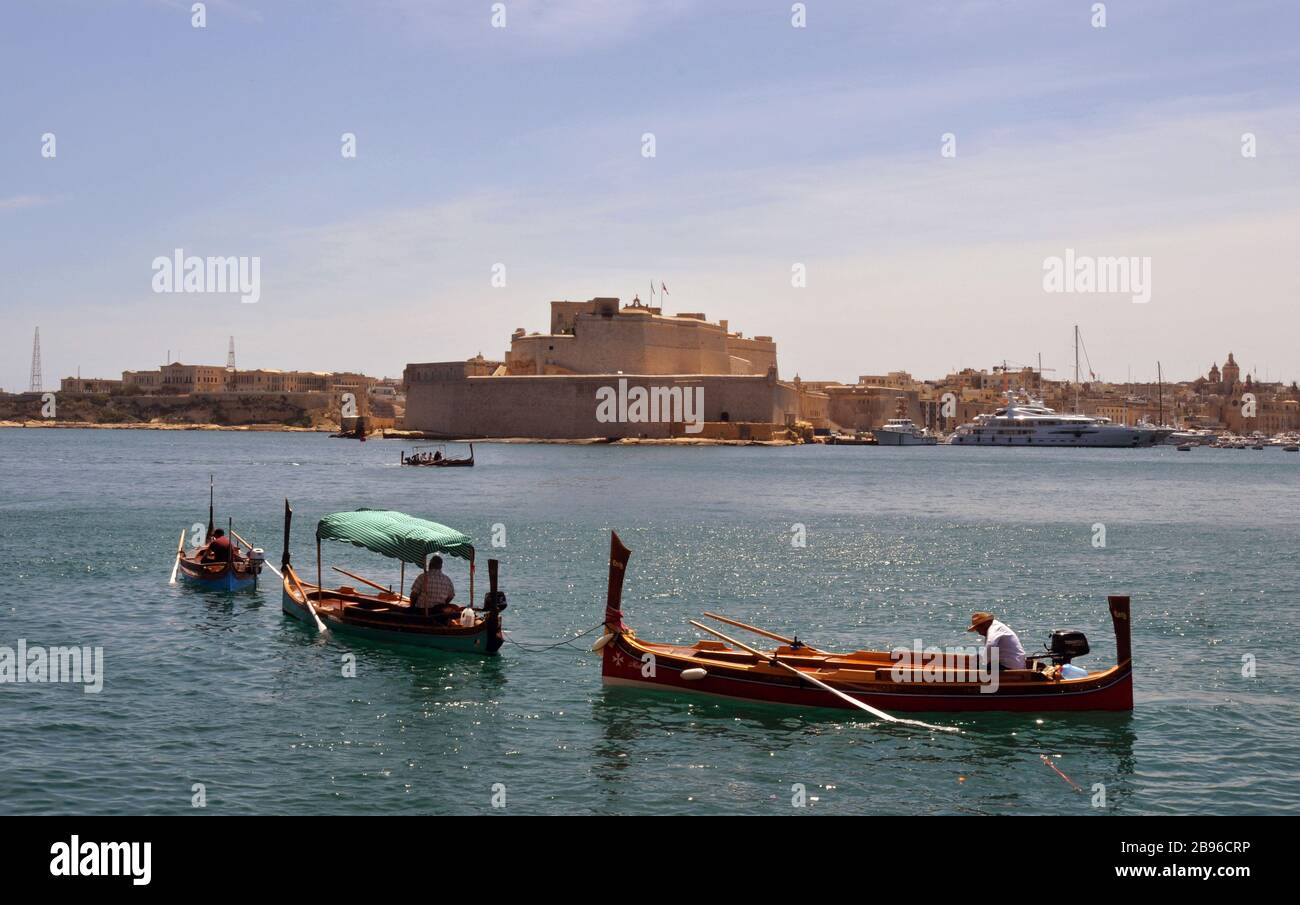 Traditional Maltese water taxis called dgħajsa set out from Valletta. Fort St. Angelo and Birgu are pictured across the Grand Harbour. Stock Photo