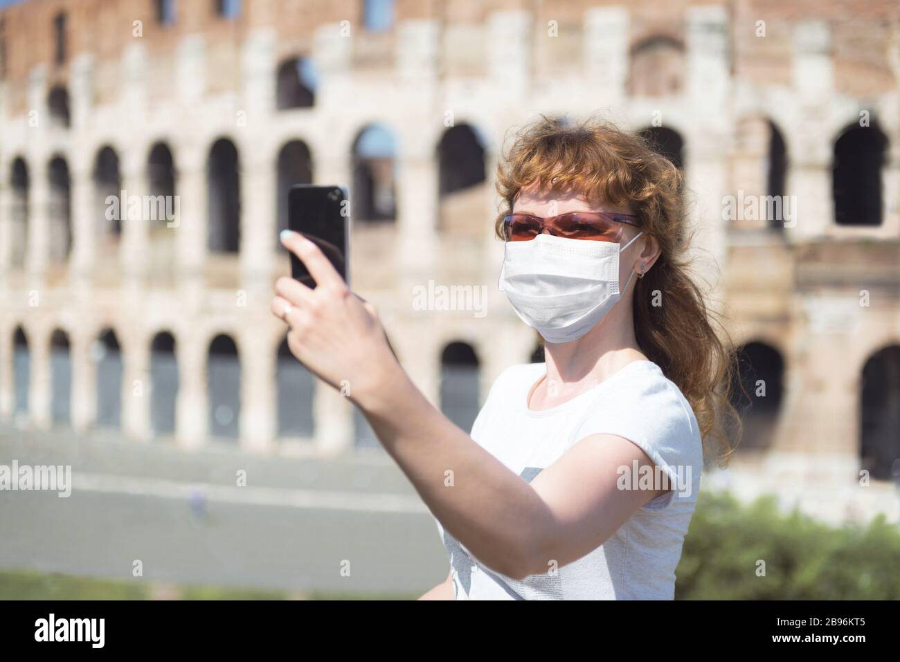 COVID-19 coronavirus in Italy, woman in protective mask makes selfie by empty Coliseum in Rome. Tourist landmarks closed due to corona virus outbreak. Stock Photo
