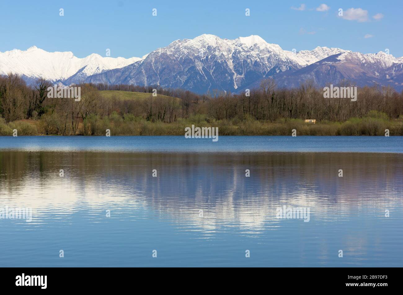 Small lake of Ragogna, near San Daniele del Friuli, Italy, in late winter, with the snow-capped mountains in the background Stock Photo