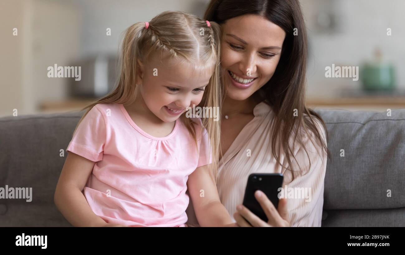 Smiling mom and little daughter using smartphone together Stock Photo ...