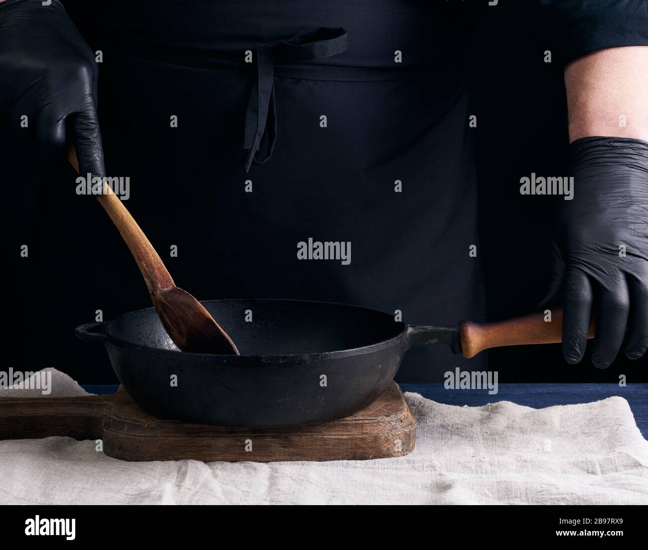 https://c8.alamy.com/comp/2B97RX9/cook-in-black-uniform-and-latex-gloves-stirs-a-vintage-wooden-spoon-food-in-a-cast-iron-pan-with-a-handle-dark-background-2B97RX9.jpg