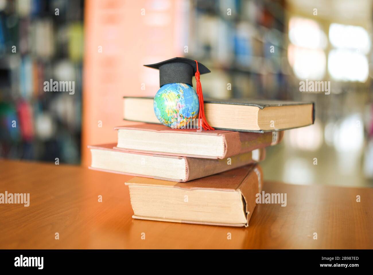 Books on the table in the library / Education learning old book stack and graduation cap on earth globe model on wood desk and blurred bookshelf room Stock Photo