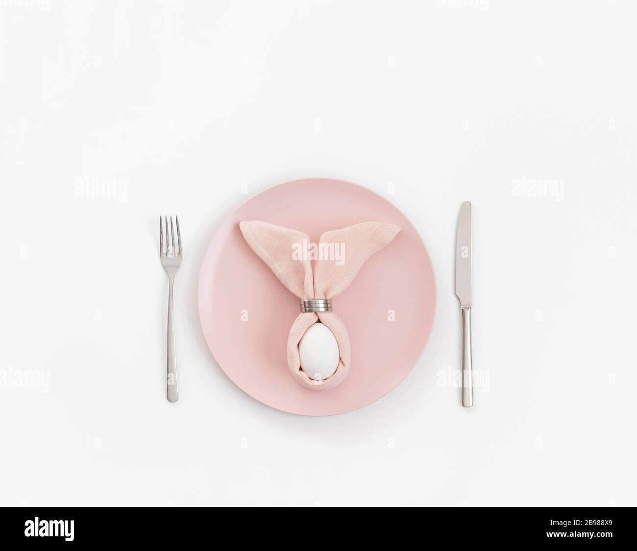 Happy easter concept. Easter table setting with egg in pink napkin Easter Bunny on a white background. Copy space, top view, flat lay. Stock Photo
