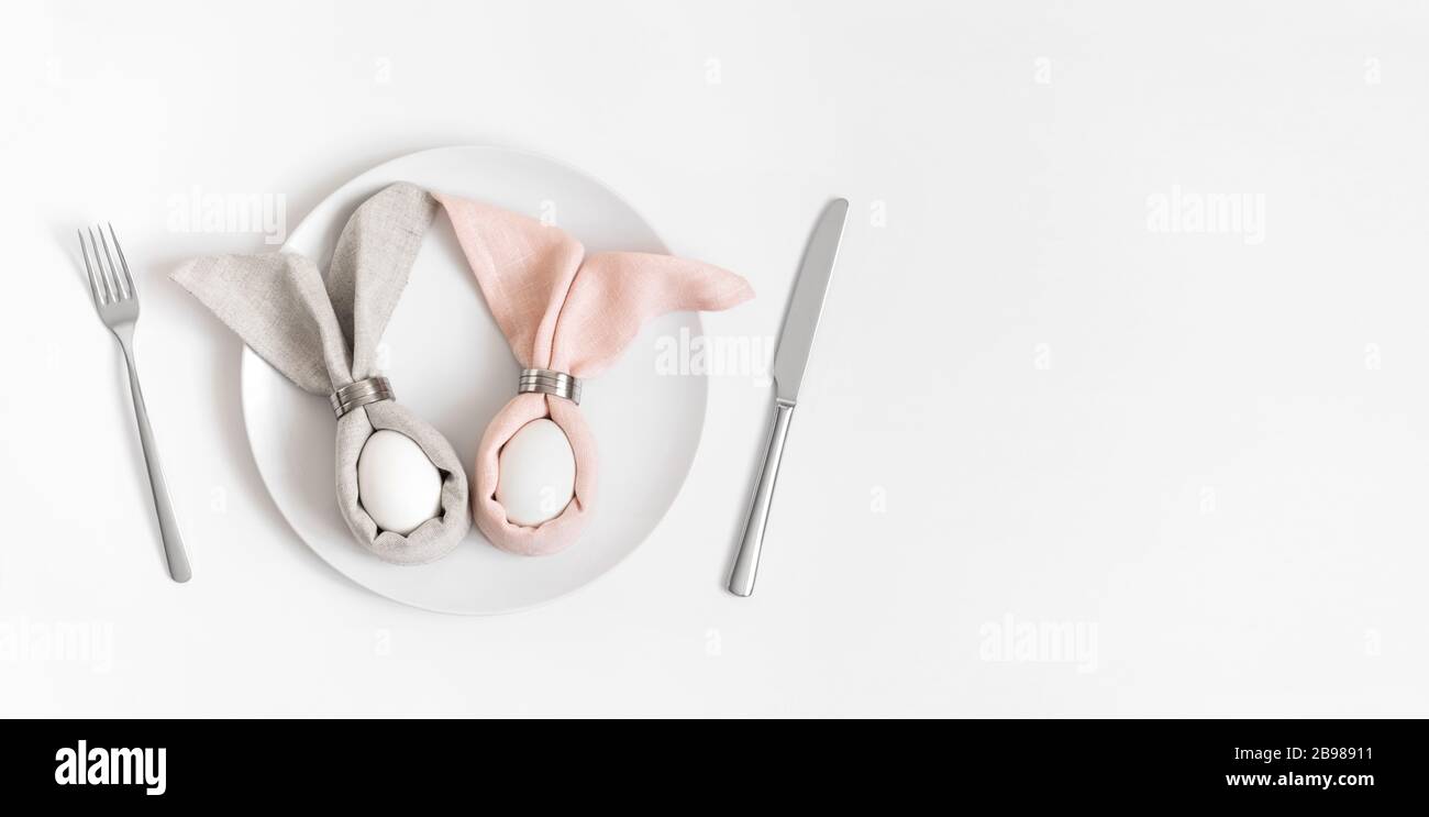 Happy easter concept. Easter table setting with egg in Easter bunny napkin on a white background. Banner. Copy space, top view, flat lay. Stock Photo