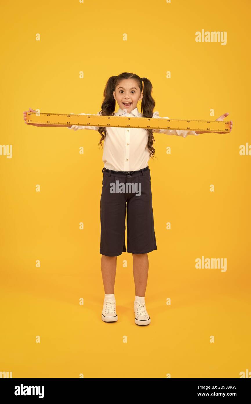 What a long ruler. Surprised little student holding rigid wooden ruler