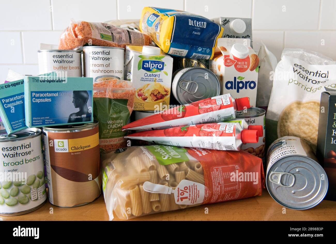 Tins and packets of dried food piled up on kitchen work surface after home delivery.  Stockpiling due to Coronavirus pandemic. Stock Photo