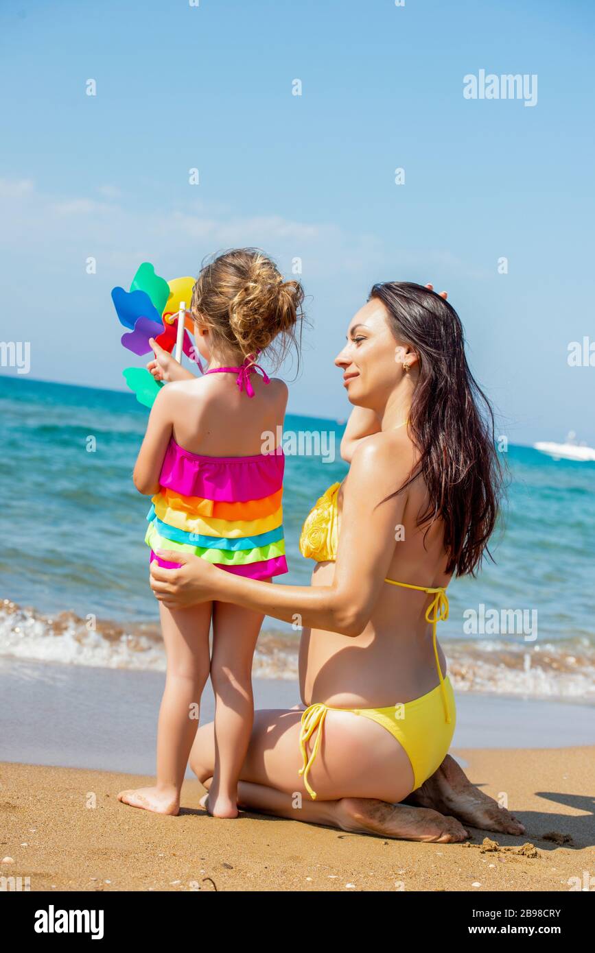 Beautiful young mother in a swimsuit and a small 3 year old daughter with a  multi-colored pinwheel rainbow on the sandy beach at sea Stock Photo - Alamy