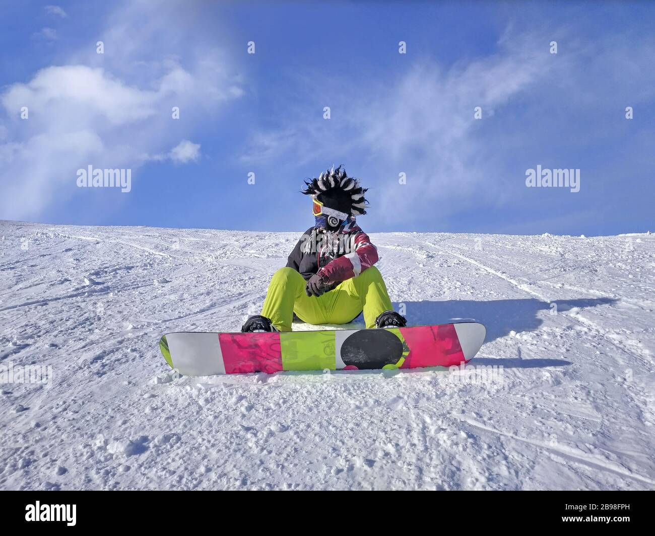 Young man - snowboarder sitting on the top of the mountain admiring the view over clouds. Sitting above the clouds. Beautiful winter nature in the Stock Photo