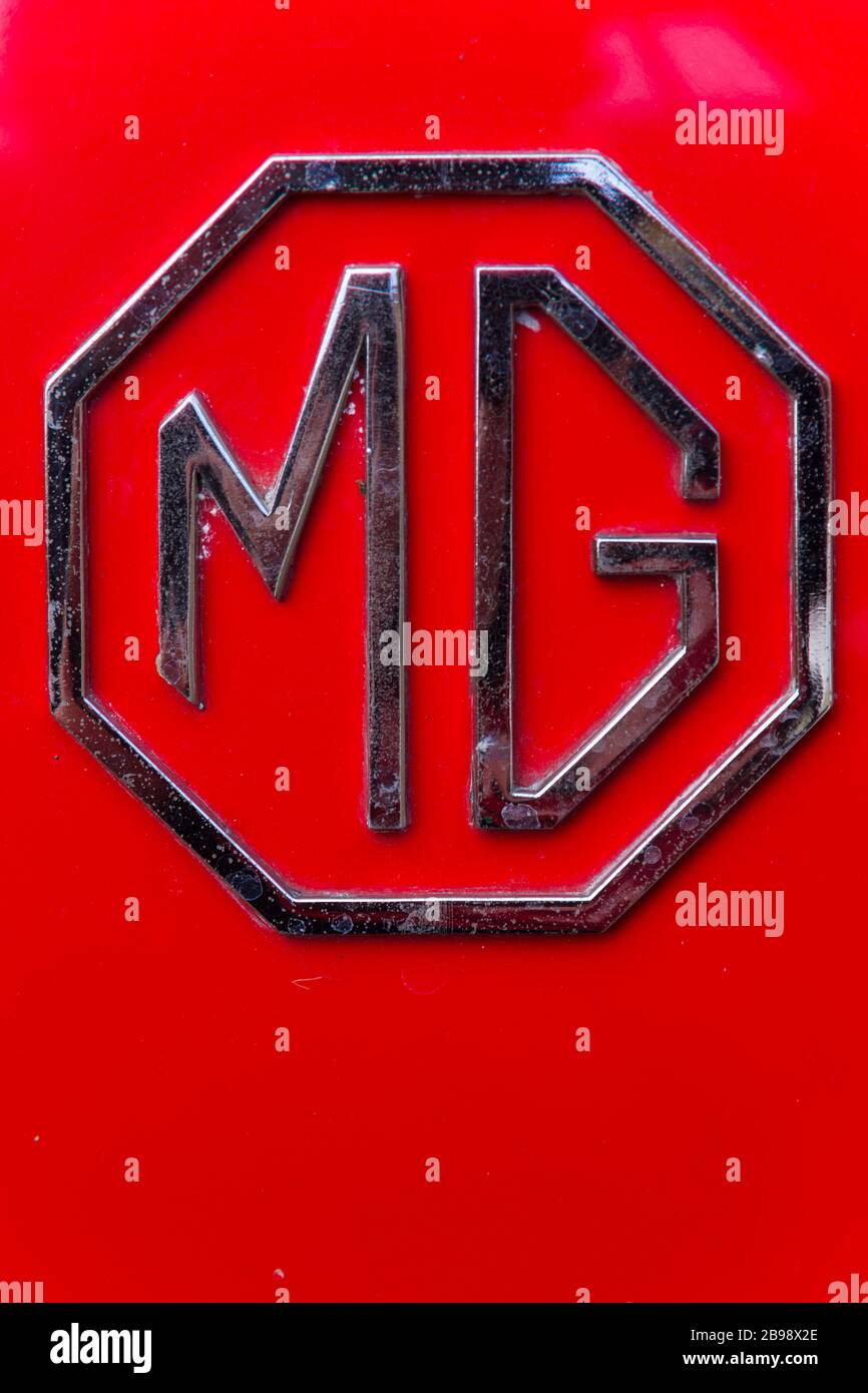 Detail of shiny chrome octagonal 'MG' bar badge on rear boot of classic red British MG sportscar displayed at car rally in Oxfordshire, United Kingdom Stock Photo