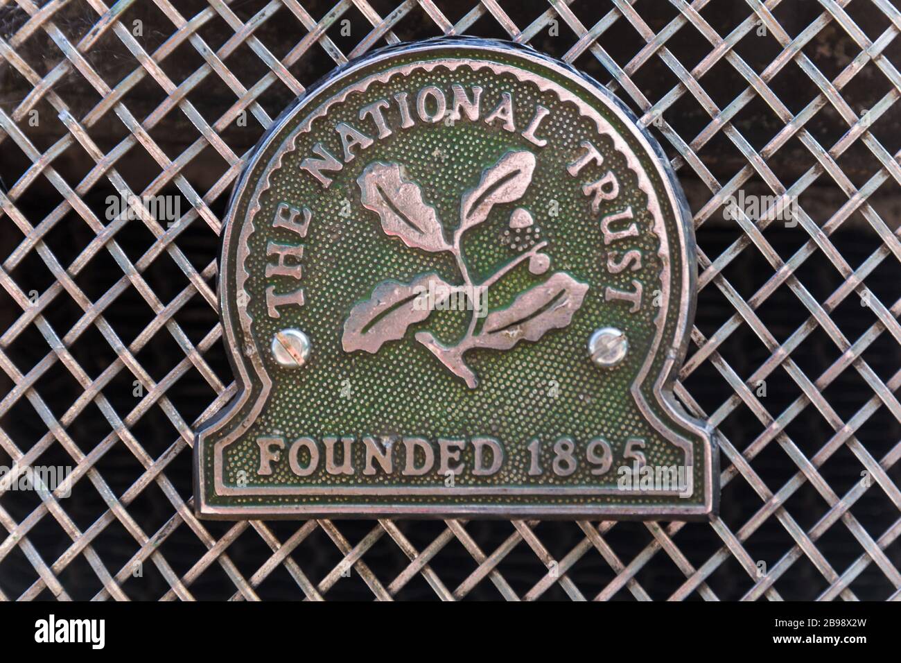 Green 'The National Trust founded 1895' vintage chrome metal car badge with oak leaf symbol mounted on wire mesh radiator grille of Austin Morris car. Stock Photo