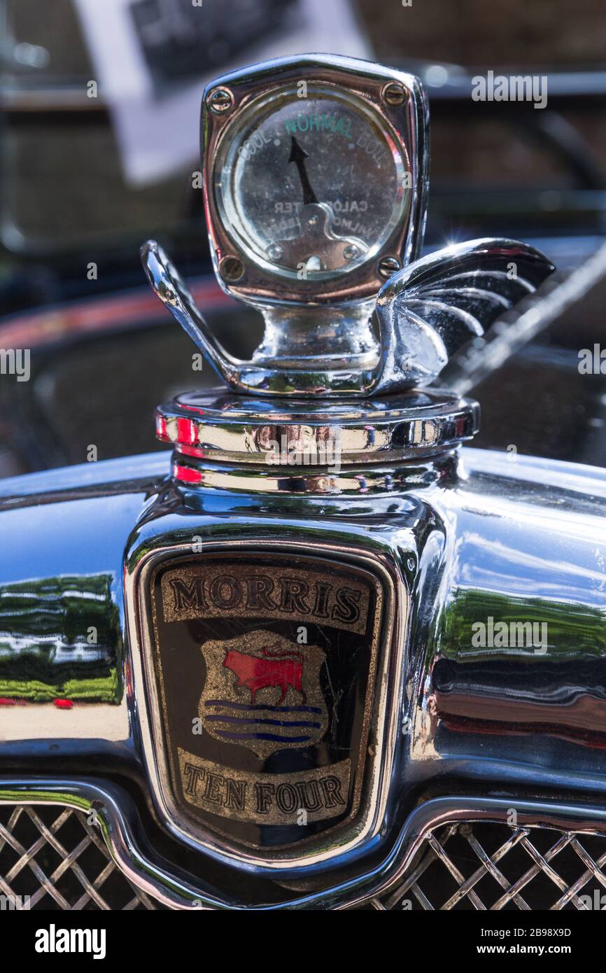 Vintage shiny polished chrome radiator badge and ornate external winged glass fronted temperature gauge cap on engine bonnet classic Morris Ten car. Stock Photo