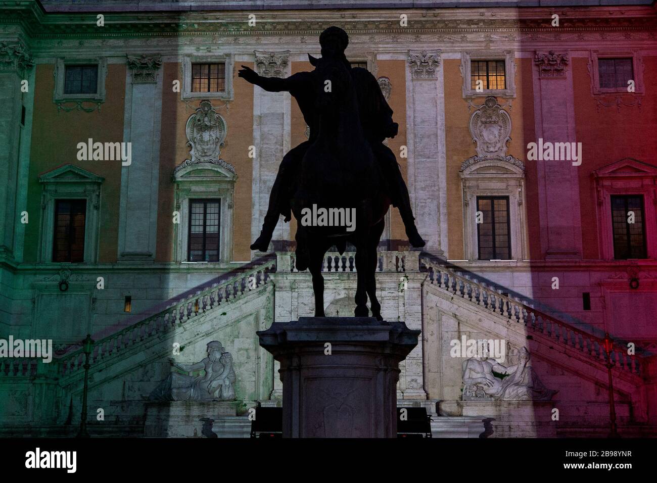 Roma, Italy. 23rd Mar, 2020. A view of Marco Aurelio statue in Piazza Del Campidoglio in Rome with the main building illuminated with the colors of the Italian flag during the 14th day of lockdown imposed nationwide by the Italian government that tries to tackle the coronavirus outbreak. Every movements in the citiies are restricted, and streets usually filled with life and traffic are almost empty (Photo by Giuseppe Fama/Pacific Press) Credit: Pacific Press Agency/Alamy Live News Stock Photo