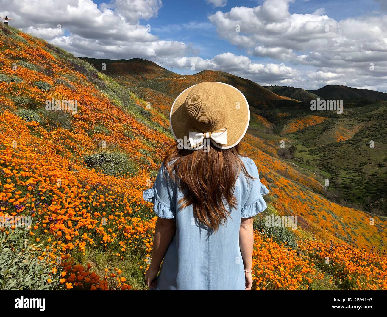 red haired girl in a blue ruffle sleeve dress and hat with bow overlooking the orange poppy superbloom in Lake Elsinore, California Stock Photo
