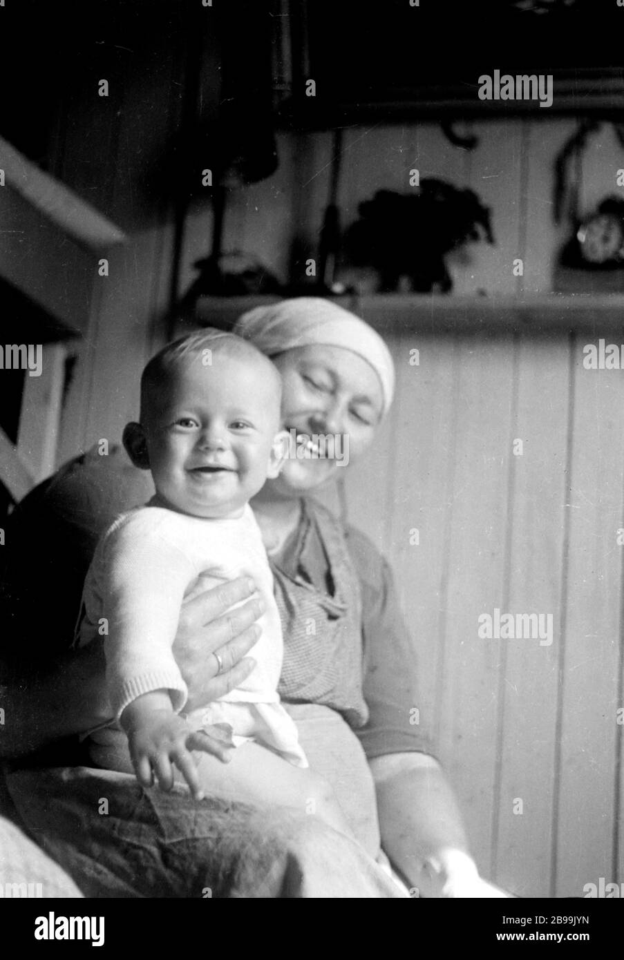 Nine month old Latvian refugee boy sits on mother's lap (both model released) in German Displaced Persons Camp after WWII. Stock Photo