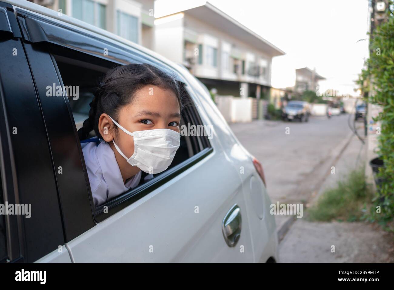 The little Asian girl pokes her head out of the car window. Hygiene mask protection coronavirus or covid-19. Students sit in a car and wear masks to p Stock Photo
