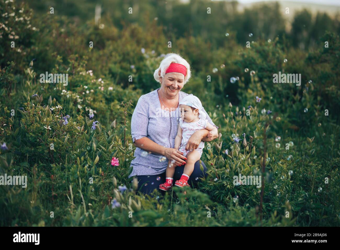 Grandmother Hugging granddaughter In nature in sunny summer day Stock Photo