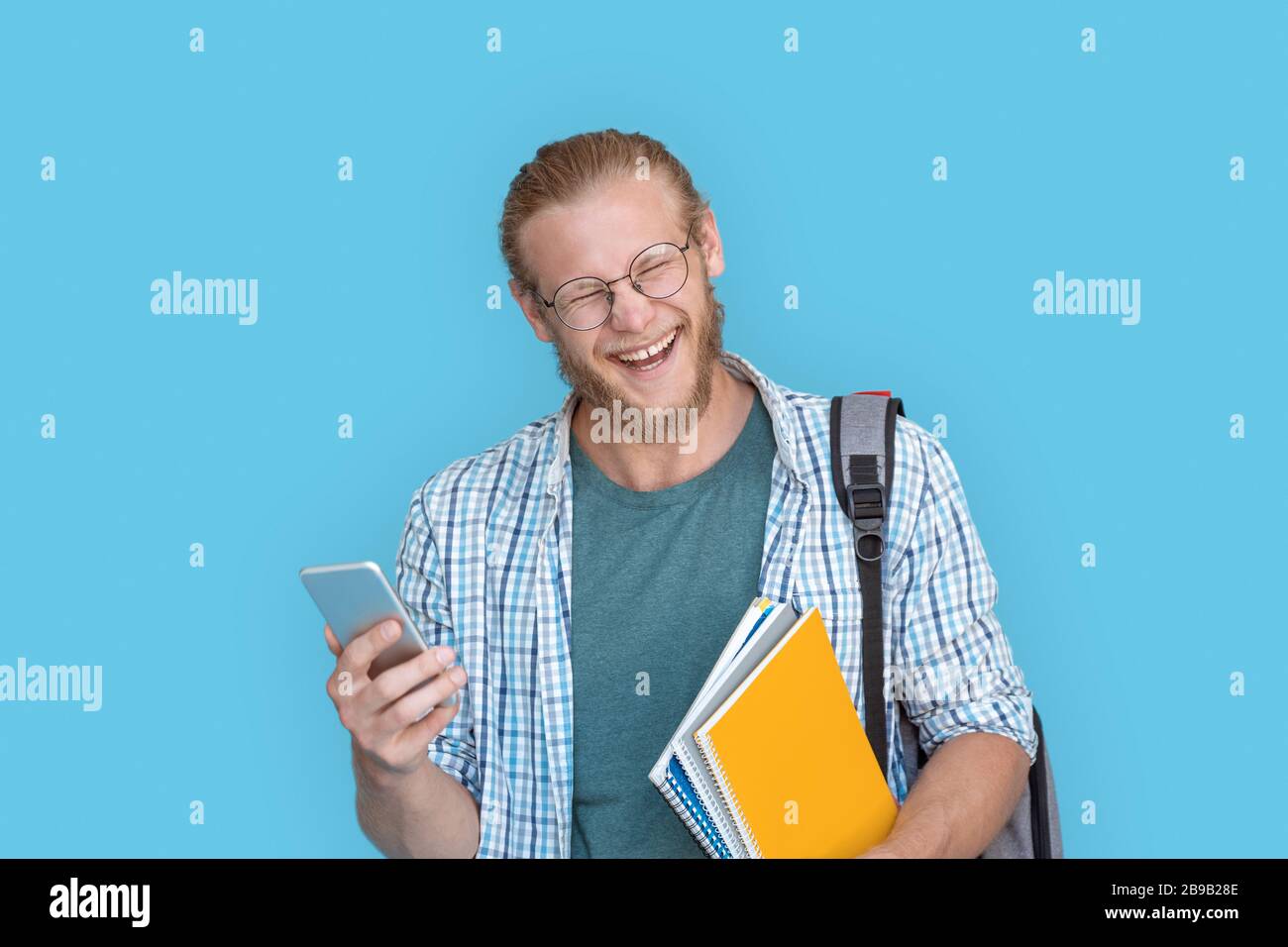 Bearded young man in glasses hold modern smartphone laughing at joke. Stock Photo