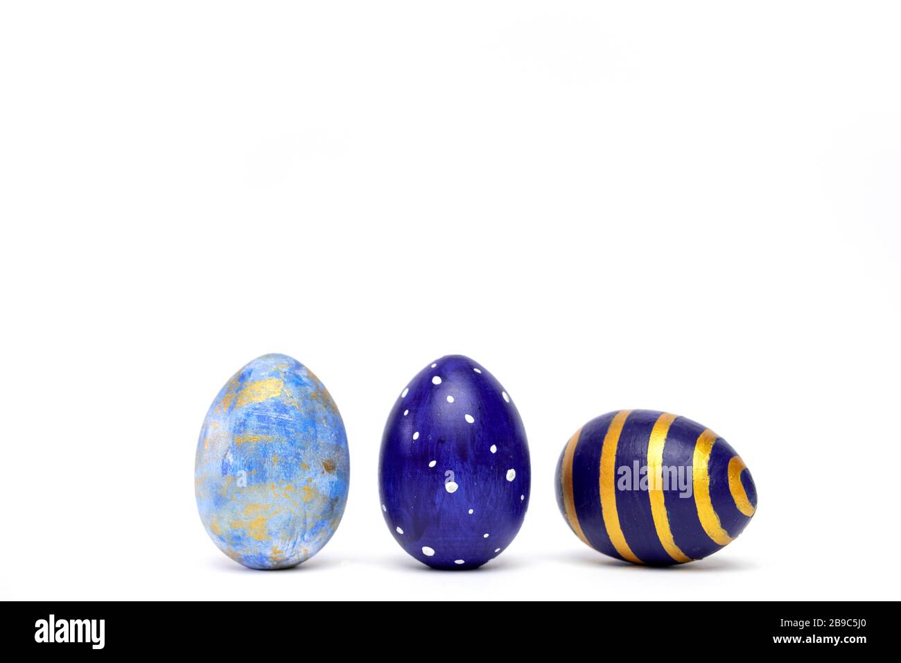 Three easter eggs trendy colored classic blue, white and golden decorated on white table. Happy Easter card with copy space for text. Minimal style Stock Photo