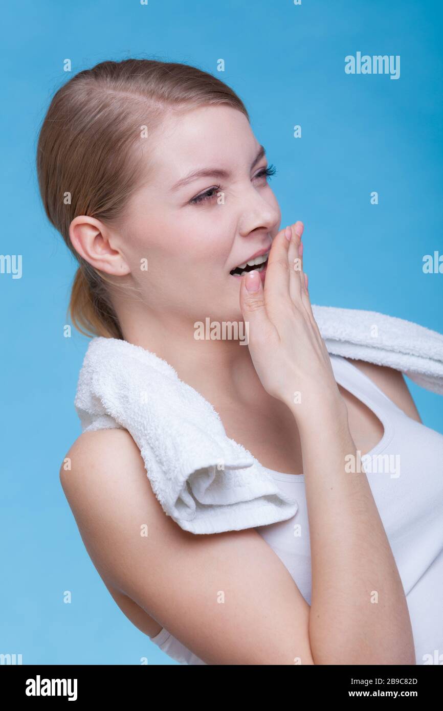 Tiredness, boredom concept. Sleepy woman placing hand on mouth yawning while holding towel on shoulder, studio shot on blue background Stock Photo