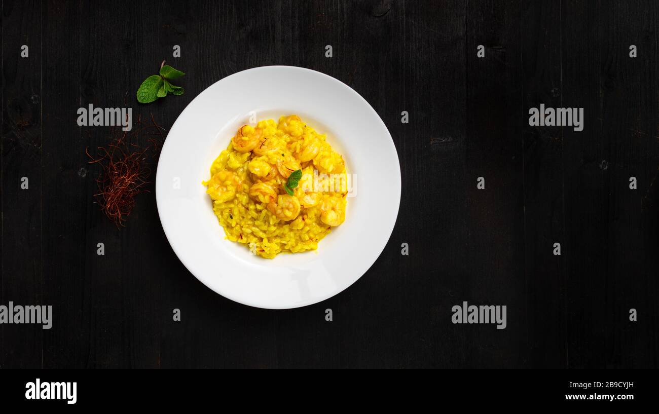 Super clean tatsy risotto with seafood and curry. Round plate and wooden background with space for text. Good as banner or cover. Stock Photo
