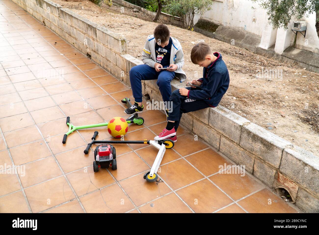 Mobile phone is a modern problem for children. Children play on the phone in the park. Toys and scooters are abandoned. Smartphone addiction in Stock Photo