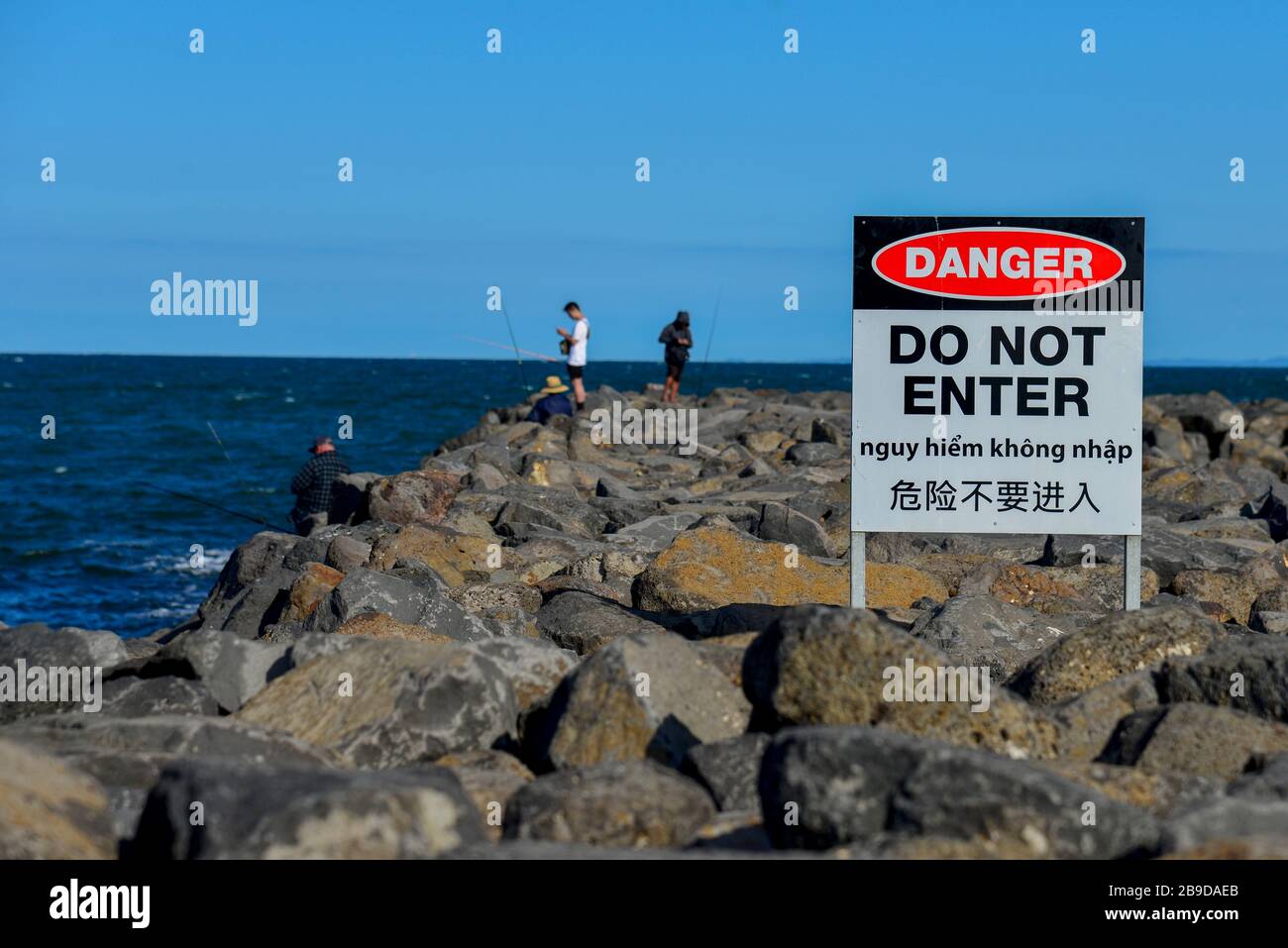 Fishermen Breaking Rules Danger Do Not Enter Sign on Breakwall Breakwater Rocks Multilingual Notice Stock Photo