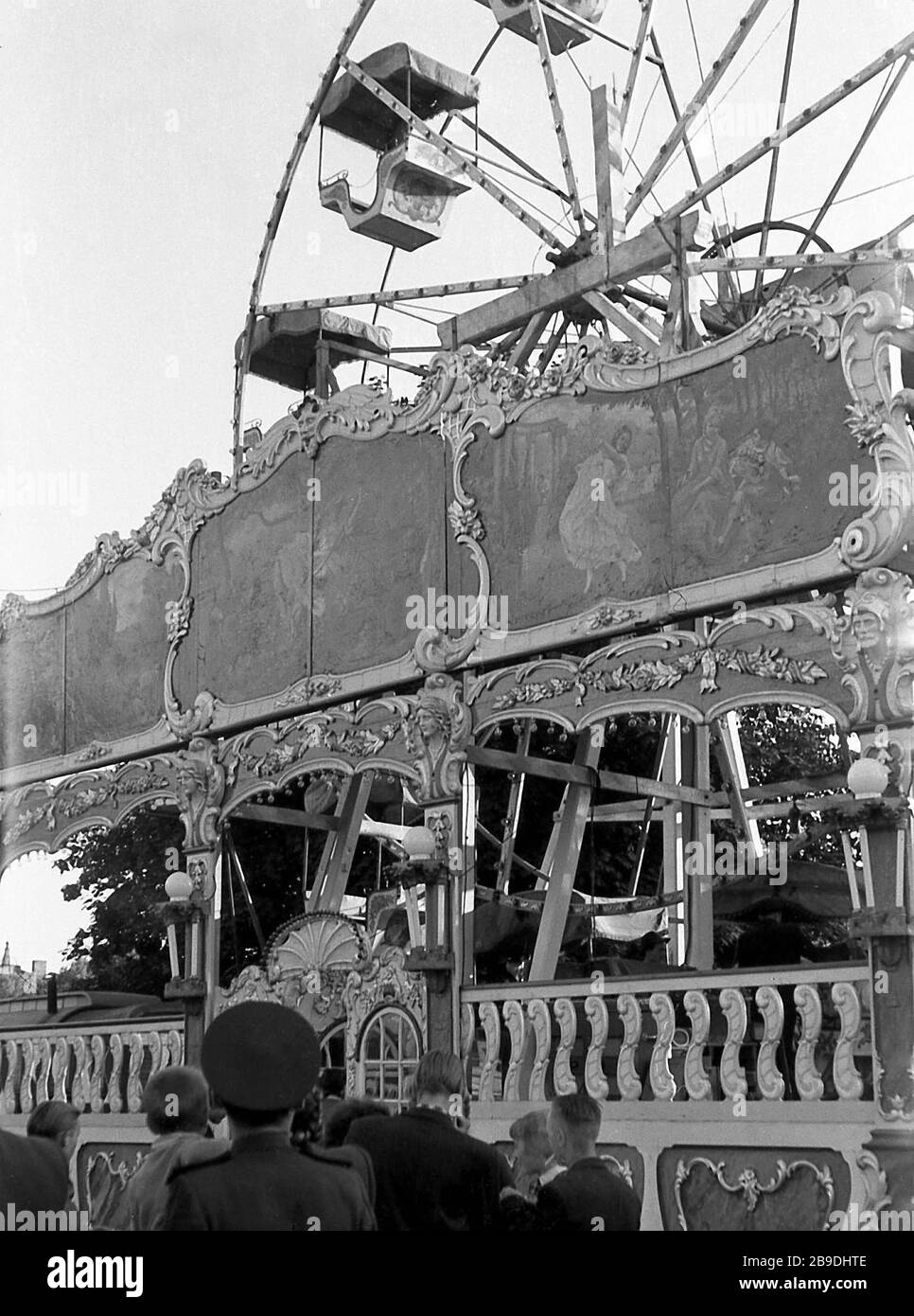 People stand in line in front of a Ferris wheel at a fairground in