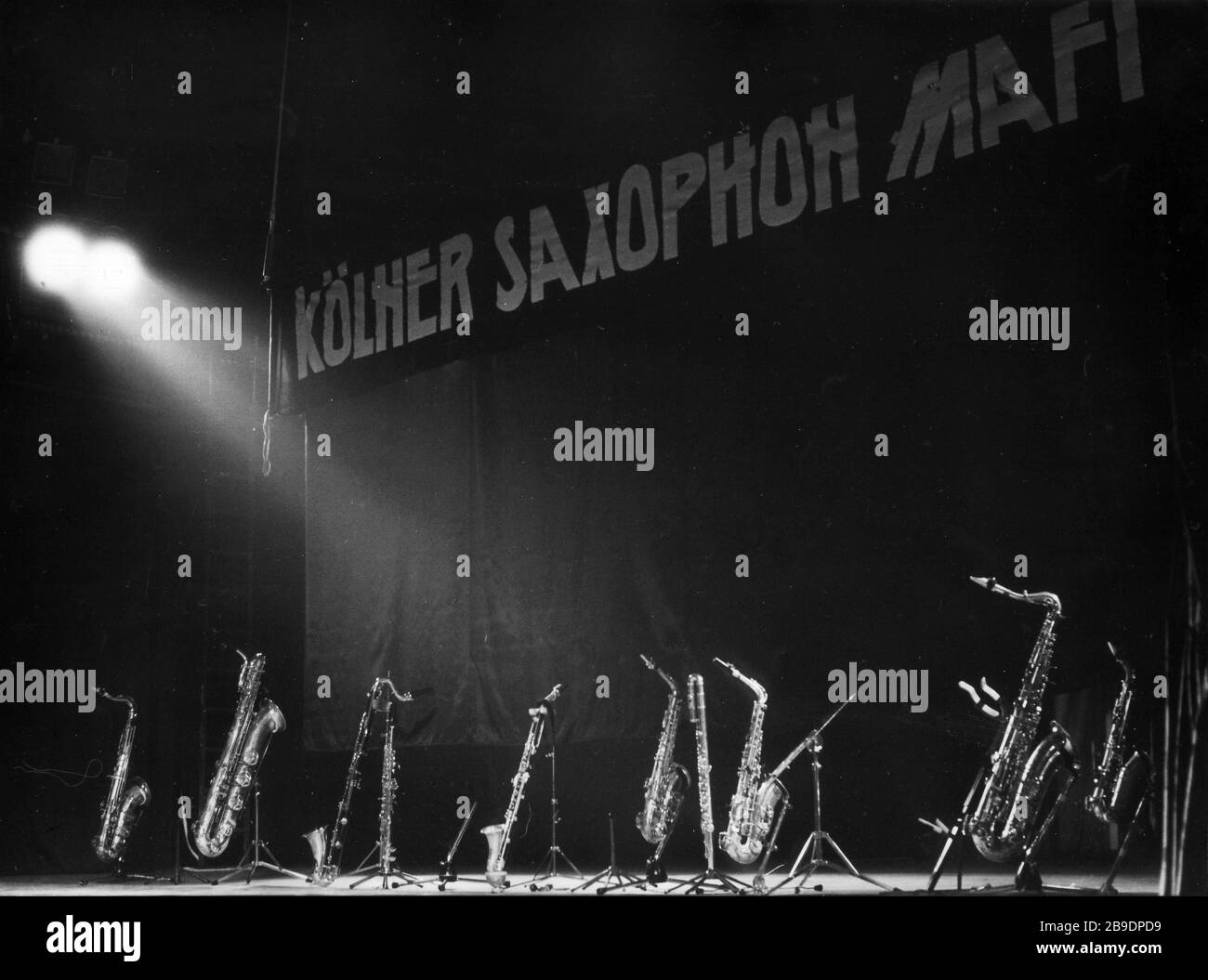 The saxophones of the jazz band 'Kölner Saxophon Mafia' are available for the musicians in their stands on the stage of the youth clubhouse in Halle an der Saale in March 1990. In the background on the curtain the name of the band. The instruments are illuminated by a spotlight. [automated translation] Stock Photo