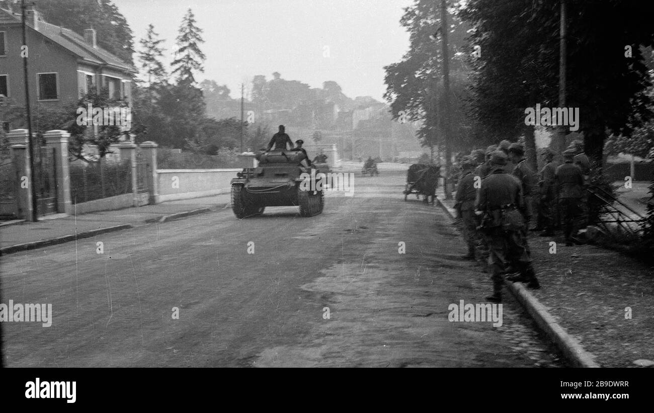 Soldiers watch a unit with Panzer II rolling through a French village ...