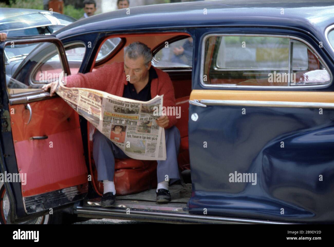 A waiting taxi driver sits in his car and reads a newspaper in Istanbul ...