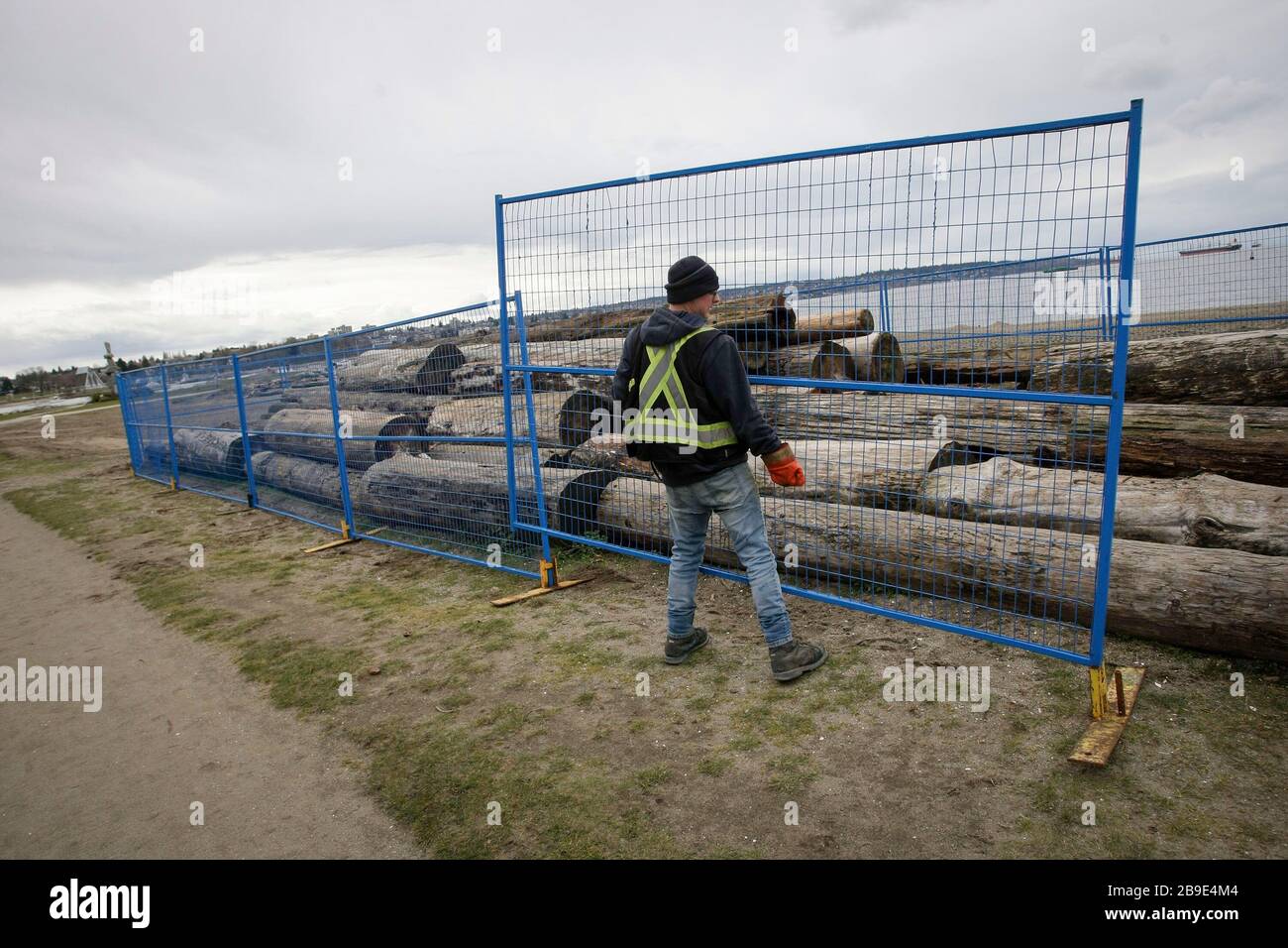Vancouver, Canada. 23rd Mar, 2020. A worker puts up fences around wood logs to prevent people from gathering at English Bay in Vancouver, Canada, March 23, 2020. Canadian Prime Minister Justin Trudeau announced Monday that his government will allot 192 million Canadian dollars (132 million U.S. dollars) on the development and production of vaccines and treatments against COVID-19. Credit: Liang Sen/Xinhua/Alamy Live News Stock Photo